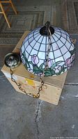 Side view of Tiffany style stained glass swag light on cardboard box showing chain and ceiling canopy.