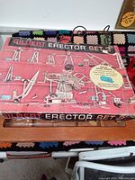 Top view of red Gilbert Erector Set 3 box featuring a boy playing with assembled erector models including cranes and vehicles. Box top has text mentioning solid steel parts and Powermatic motor.