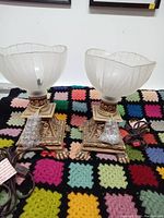 Photo showing both glass lamps side by side on a multicolor patchwork blanket background, highlighting the brass bases and frosted glass shades.