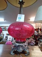 Close-up of one pink glass lamp with crackled glass base and ornate silver tone metal stand, showing detailed scrollwork and floral pattern on the stand.