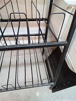Close-up side view of the black metal pipe comic rack showing wire dividers for comics and metal frame structure.