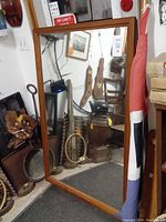 Front view of a large rectangular mirror with a wooden frame surrounded by various items on the floor and walls.
