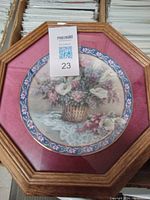 Framed ceramic plate featuring a basket of flowers including calla lilies, with decorative blue and pink floral border and pink matting