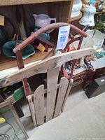 Side view of metal frame toboggan showing red metal curved frame and wooden slat seating area.