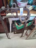 Two metal hay grabbers with clamp-style handles and long prongs for grabbing hay.