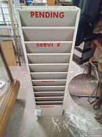 Full front view of the metal service rack showing compartments labeled Pending, Service, Neon, Install, Comics etc.