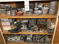 Wide view of three shelves filled with various metal baking molds including stackable cupcake pans, tart pans, round and oval baking molds, and animal cake molds.