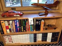 Shelf with books, model airplane on stand, red sports car and wooden convertible car visible