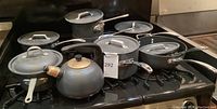 Seven pieces of grey commercial aluminum cookware arranged on a stove; includes three saucepans, two stock pots, one sauté pan and one kettle