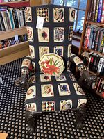 Front three-quarter view of chair upholstered in playing card motif fabric with included floral needlepoint cushion