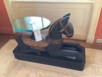 Side view of carved wooden horse base with oval glass top and metal support