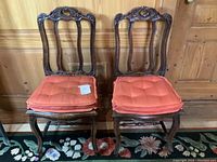 Pair of vintage carved wooden chairs with red-orange cushions positioned side by side showing front and detail of woodwork.