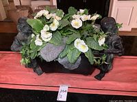 Front view of cast iron planter with two kneeling figures supporting rectangular basin, filled with flowers
