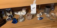 Shelf view with assorted items including pewter stein, white ceramic bird, framed butterflies, glass dishes