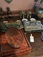 Full view of wooden trays of different shapes and sizes stacked, with two carved wooden elephant figures, and vintage desk writing set partially visible on a wooden table.