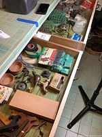 Overview of drawer showing wooden plate easels, floral supplies, brass faucet, tape and other hardware