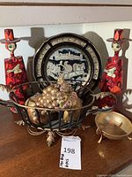 Overall view of the lot showing Greek plate, metal basket with faux fruit, small metal dish and two red folk art figurines