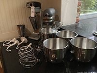 Wide view showing both mixers, three bowls, pouring shield and attachments arranged on table