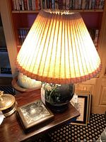 Full view of ceramic lamp with pleated lampshade and square leather ashtray on wooden table