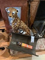 Front view of large ceramic leopard statue sitting next to metal firewood holder.
