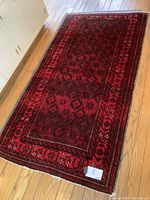 Full view of hand loom made red and black rug placed on wooden floor, showing entire rug and pattern details.