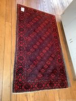 Photo of full red and black loom made rug laid flat on wooden floor