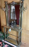 Full front view of metal hall tree console with mirror, two easels on top shelf, faux plant at base