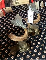 Pair of brass-tone dolphin brackets on patterned carpet with books in background.