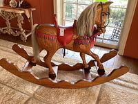 Full side view of carved wooden rocking horse on curved rockers with red saddle and natural wood grain