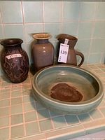 All four items grouped on tiled surface: carved vase, crackle-glaze vase, pitcher, green bowl