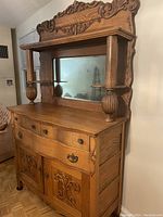 Front side view of antique oak buffet showcasing carved wood details and mirror.