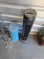 Photo of two tower fans side by side, one black Hawaiian Breeze fan and one smaller blue fan, showing overall condition and size.