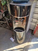 Full view of one standing water dispenser with dual spouts and drip tray on bottom.