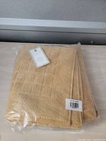 Clear image of the sealed beige bath mat showing texture, folded neatly on table.