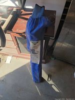 Photo of the folding chair in the closed carry bag standing upright indoors with sunlight.