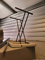 Side profile photo of the folding table folded with black metal legs extended upward, showing the textured edge of the beige plastic tabletop.