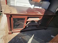 Full view of the wooden TV stand showing two glass cabinet doors and open shelving, dusty top surface