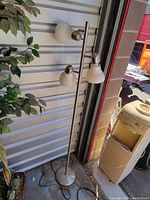 Full view of floor lamp with three adjustable light heads, standing next to a water cooler and a plant.