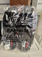 Clear plastic bag with a visible pair of black Alpine Swiss sandals inside, showing the brand logos and packaging.