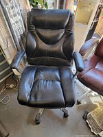 Front view of black faux leather office chair with cushioned seat and armrests showing wear and use.