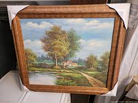Framed oil on canvas painting of a rural landscape with trees, pond, path, and house in the distance.