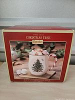 Box front showing Spode Christmas Tree mug with peppermint candy cane handle filled with hot chocolate and marshmallows.
