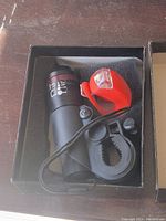 Top view of the black front LED bicycle light, orange rear light, mounting clip, and wrist strap inside the original box.