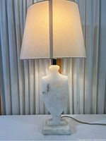 Full view of the vintage white vein stone table lamp with white fabric lampshade against a vertically striped backdrop.