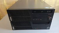 Two Lenovo ThinkCentre computer towers stacked horizontally, front panel view showing ports, buttons, and optical drive slot.