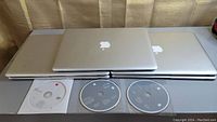 Five MacBook Air laptops stacked and laid out with three Apple software discs visible in front.