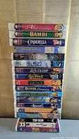 Stack of 18 VHS tapes with visible colorful spines showing titles mainly classic Disney animated movies and some others, two factory sealed