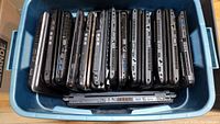 Top-down view of 14 Toshiba laptops arranged vertically inside a blue Rubbermaid container, showing the sides with multiple ports.