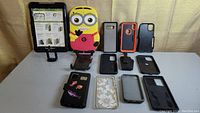 Full display of all cellphone cases, tablet case with instructional insert, Minion novelty case, and accessory stand.