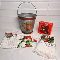 Photo of all lot items laid out showing pail, napkin rings box, and two snowman decorated kitchen linens